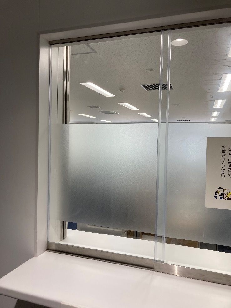 福岡市中央区受付窓ガラスに透明ガラス5㎜厚 四方糸面フチ磨き加工 室内側引き手掘り加工1箇所 外側全面透明飛散防止フィルム貼り 室内側フロストフィルム部分貼りを入れ替えた施工後の様子